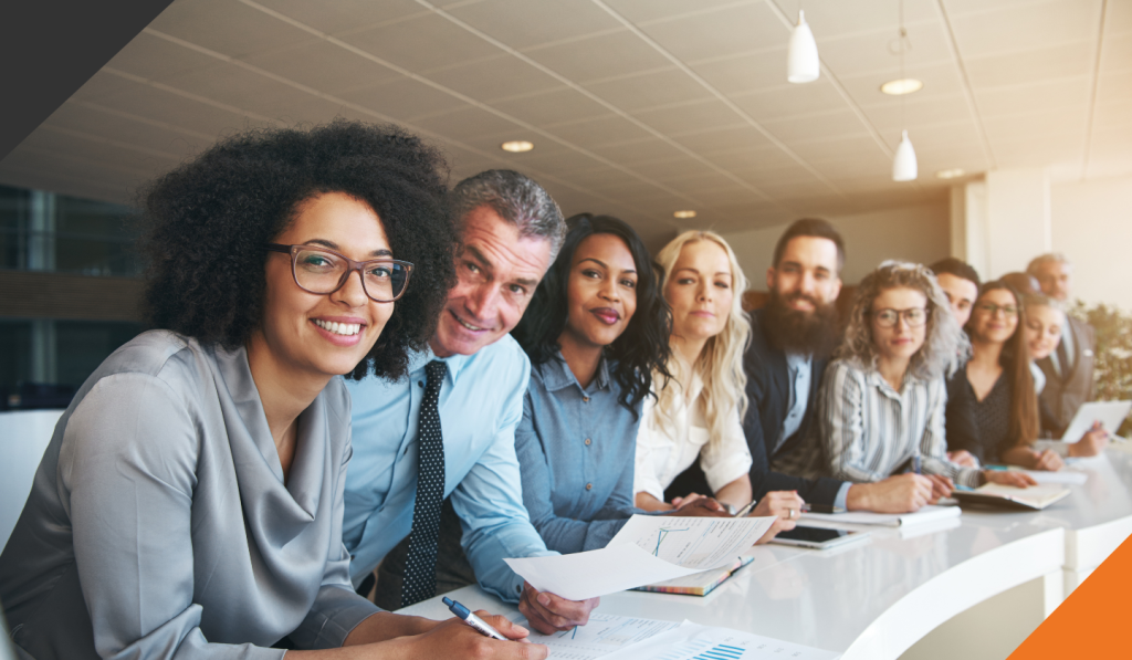 10 people of multiple ethnicities, genders and various ages leaning on a a table side by side in an office setting representing diversity, equality and inclusion