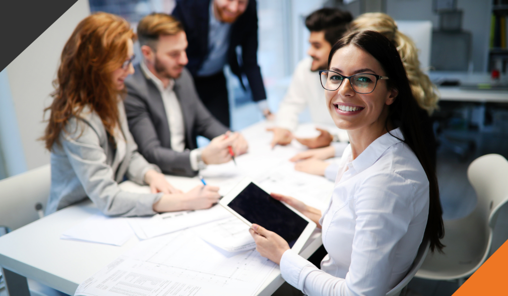 Five employees at a desk one employee facing forward smiling and displaying resilience at work, 3 examples